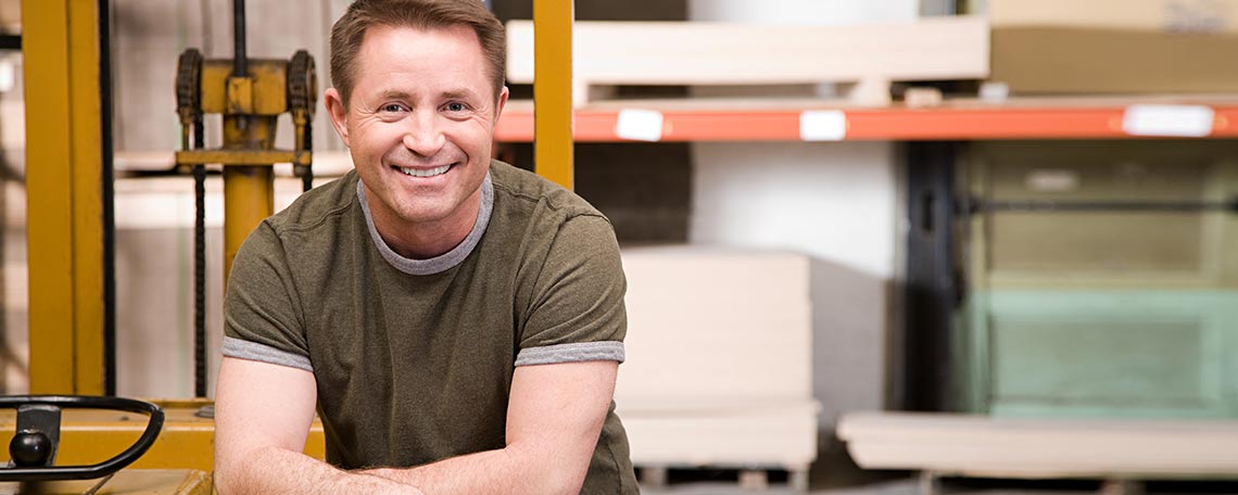 Lächelnder Lagerarbeiter mit Hubwagen in industrieller Umgebung