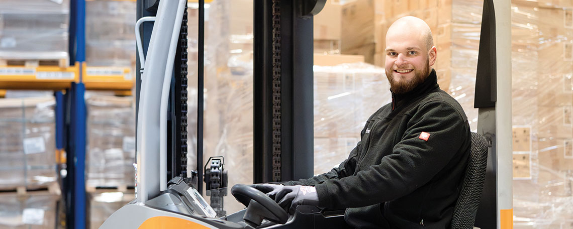 Ein Mann sitzt auf einem Gabelstapler in einer Lagerhalle mit gestapelten Paletten